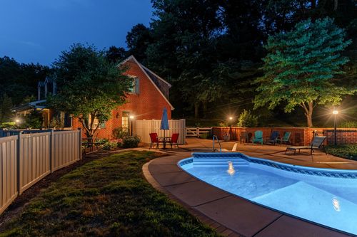 Twilight backyard with round pool, brick house, and lounge chairs on a patio