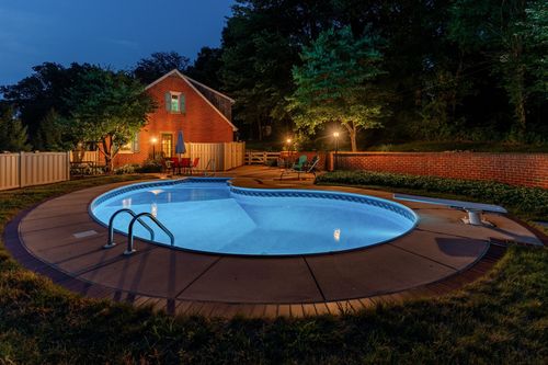 Nighttime view of a round pool with a diving board beside a lit brick home