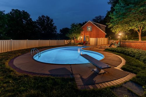 Round pool at dusk with a diving board, patio furniture, and a wood privacy fence
