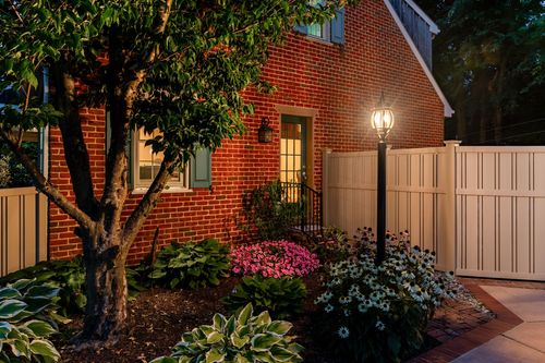 Brick home exterior at dusk with a lamppost, flowering shrubs, and a side entry