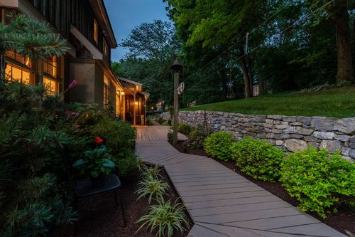 Twilight walkway lit by a lantern post leading past a stone retaining wall