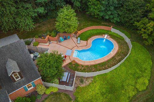 Aerial dusk view of a brick home with a curved pool and stone patio in the backyard