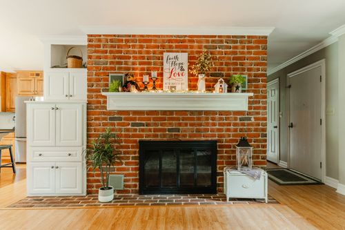 Brick fireplace with white mantel between white cabinetry and a hardwood entry