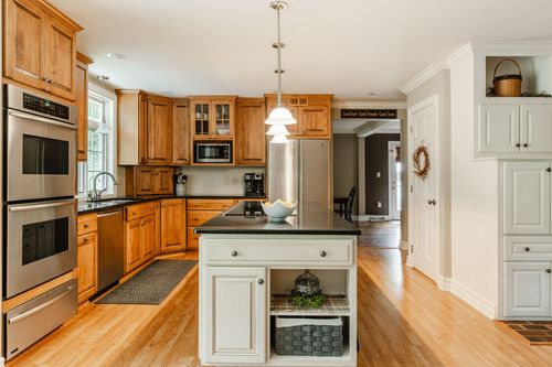 Kitchen with wood cabinetry, double wall ovens, and a black granite center island