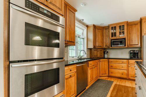 Kitchen with stacked stainless double ovens and wood cabinetry with granite counters