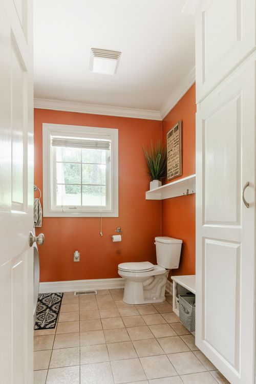 Half bath with terracotta walls, white toilet, and a window with tile flooring