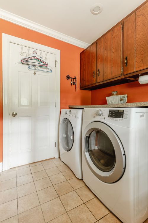 Laundry room with terracotta walls, wood cabinets, and a front-load washer dryer set