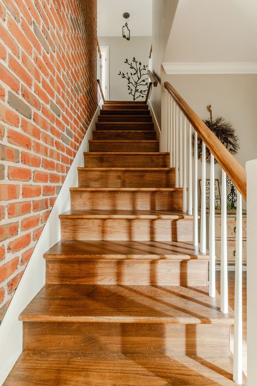 Wood staircase along an exposed brick wall with white balusters and a wood railing
