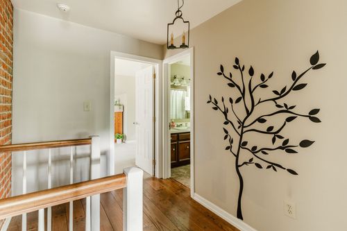 Upstairs hallway with a tree wall decal, wood floors, and a view into a bathroom