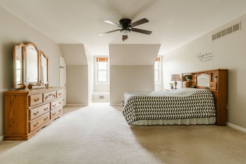 Bedroom with a ceiling fan, oak dresser with mirror, and a chevron patterned bedspread