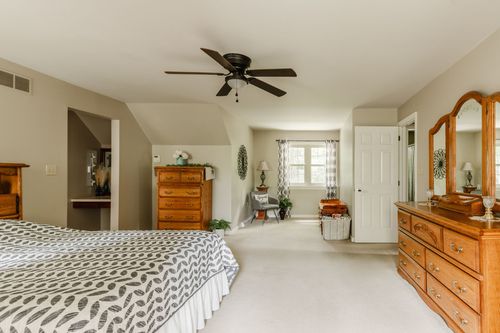 Bedroom with ceiling fan, oak dresser, sitting area, and wall-to-wall carpet