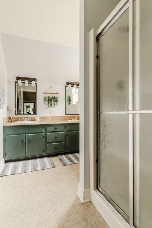 Bathroom with green vanity cabinets, marble counters, and a frosted glass shower door