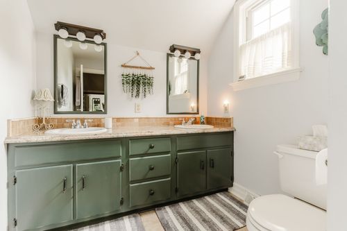 Double-sink bathroom with green cabinetry, tile backsplash, and a window
