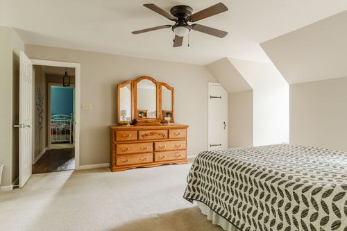 Bedroom with ceiling fan, oak dresser with mirror, and neutral carpet flooring
