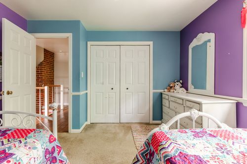 Kids bedroom with purple walls, twin beds, white closet doors, and a dresser