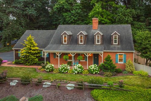 Covered brick porch with green shutters, hanging ferns, and a stone walkway