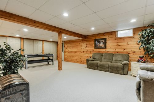 Finished basement with knotty pine walls, exposed beam, and a leather sofa