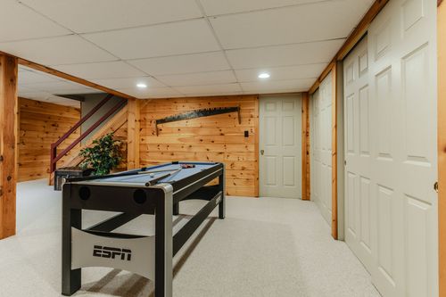 Basement game room with air hockey table, pine paneling, and a staircase