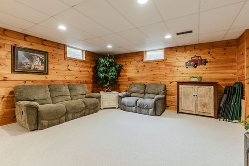 Basement family room with pine paneled walls, leather recliners, and a potted plant