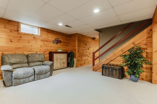 Basement lounge with a loveseat, pine walls, a wood staircase, and a storage trunk