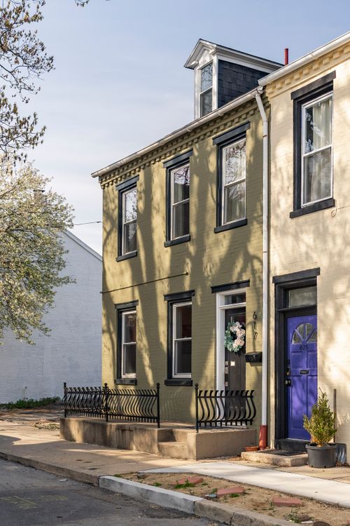 Olive-painted rowhome facade with black trim, wrought iron railing, and a wreathed door