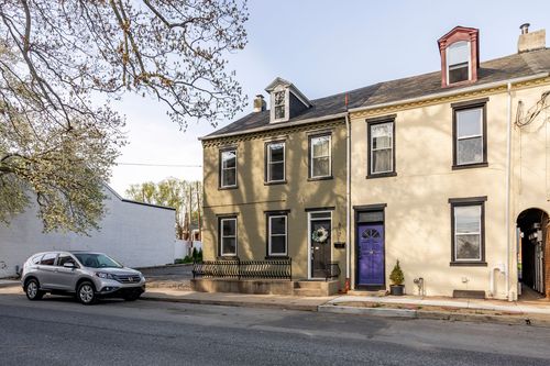 Street view of an olive brick rowhome with black trim and a purple front door next door