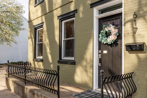 Front entrance of an olive rowhome with black trim, wrought iron railings, and a wreath