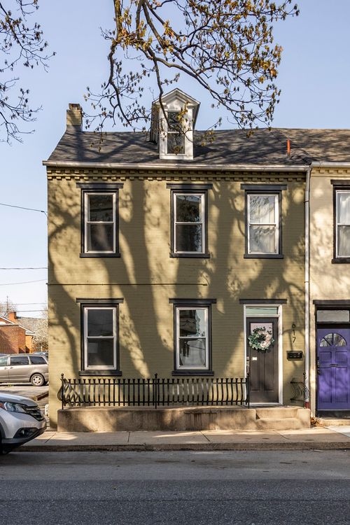 Street view of an olive brick rowhome with black window trim and wrought iron fencing