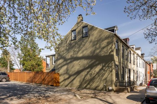 Side view of an olive rowhome with dormer windows and a wood privacy fence