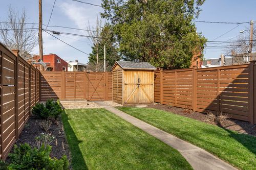 Fenced backyard with a concrete path leading to a wood storage shed and lawn