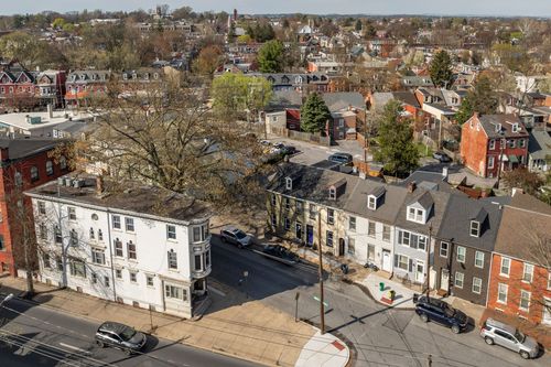 Aerial view of a city block with brick rowhomes, parked cars, and scattered trees