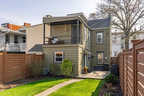 Rear exterior with a screened upper balcony, wood fencing, and a small patio