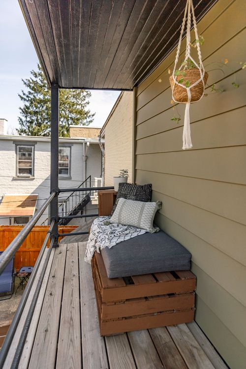 Covered balcony seating nook with a crate bench, cushions, and a hanging plant