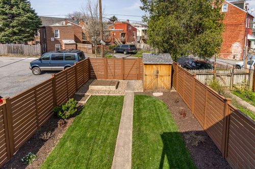 Aerial view of a fenced backyard with a storage shed and concrete walkway to the lawn