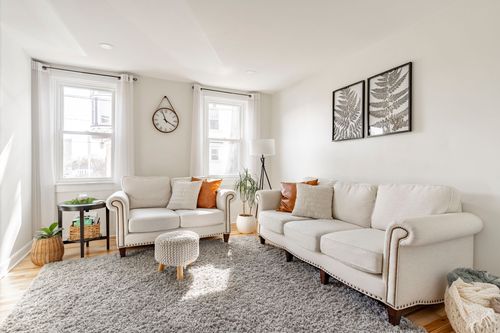 Living room with matching cream sofas, a round pouf ottoman, and bay windows
