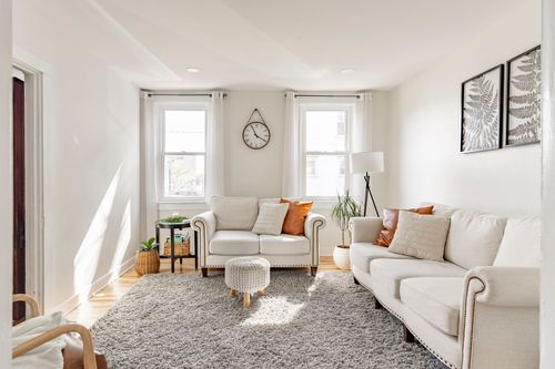 Bright living room with cream loveseat and sofa, a wall clock, and a shag rug