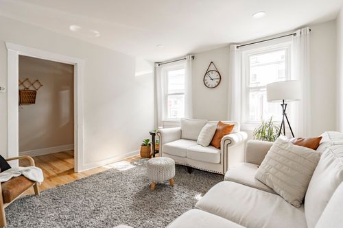 Living room with cream sofas, fern art, and a doorway opening to a hallway