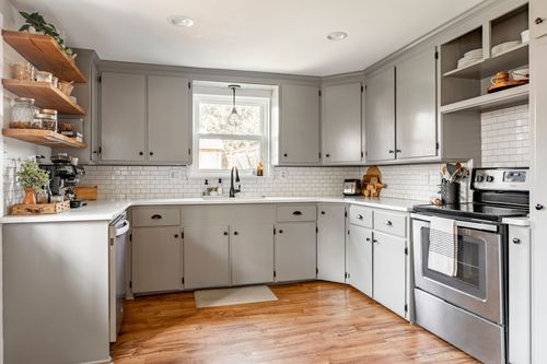 Kitchen with gray cabinetry, subway tile, open wood shelving, and a garden window