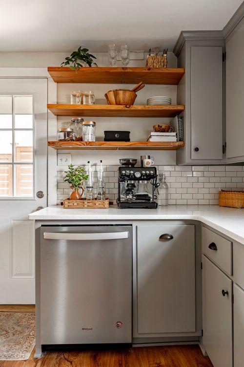 Kitchen corner with open wood shelving, subway tile, and a stainless dishwasher