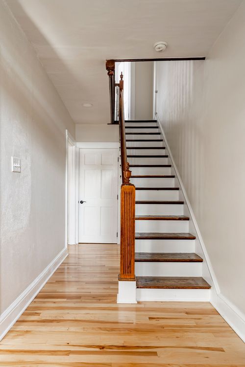 Hallway with hardwood floors leading to a wood staircase with a turned newel post
