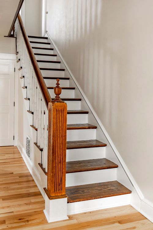 Wood staircase with white risers, a turned newel post, and painted balusters