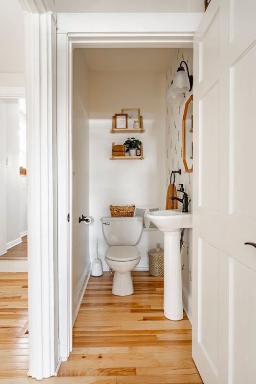 Small powder room with floral wallpaper, open shelving, and a pedestal sink