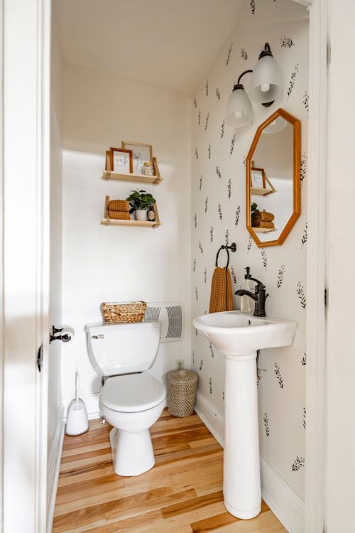Powder room with black-and-white floral wallpaper, sconce lighting, and a hex mirror