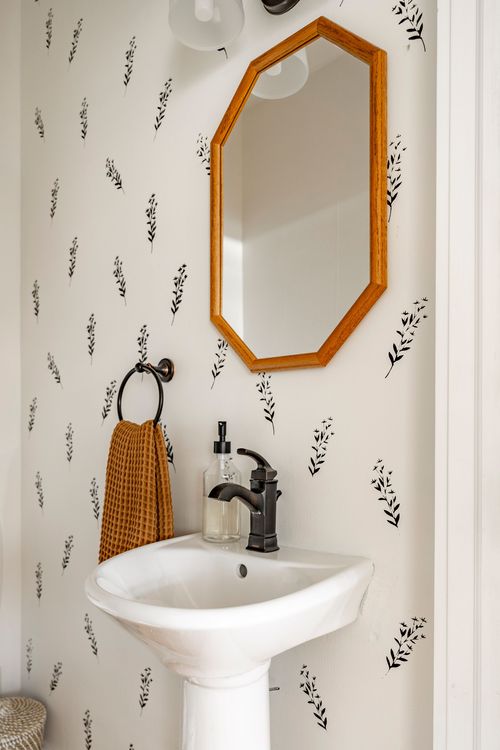 Pedestal sink detail with a hexagonal wood mirror and floral wallpaper backdrop
