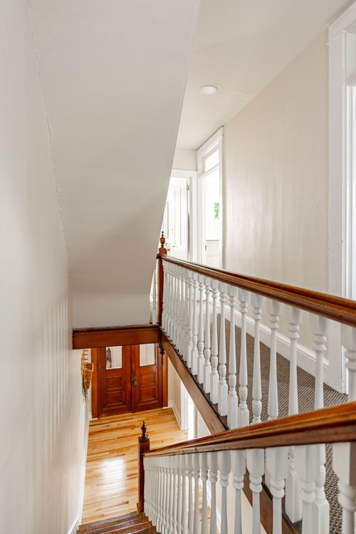 Upper staircase landing with white balusters and a wood banister overlooking the foyer