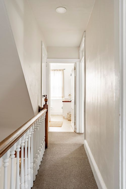 Upstairs hallway with a wood banister leading to a bathroom doorway