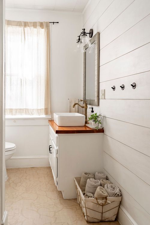 Bathroom with white vessel sink, wood countertop, shiplap walls, and towel hooks