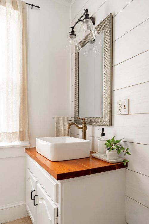 Bathroom vanity with a square vessel sink, brass faucet, and a wood countertop