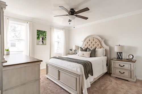 Neutral bedroom with a tufted cream headboard, ceiling fan and matching nightstands.