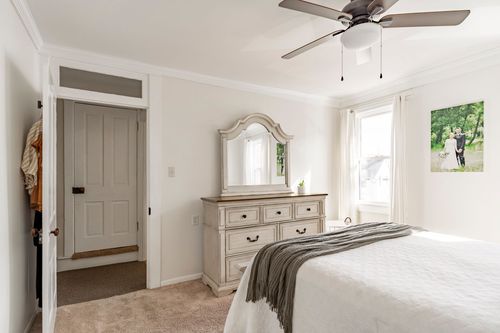 Bedroom with an arched dresser mirror, plush carpet and a gray throw folded on the bed.